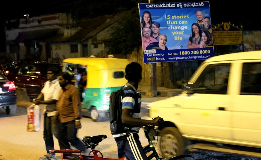 Street scene in Bangalore with a Mega City Media Campaign billboard advertising a toll-free number to call for a free book.