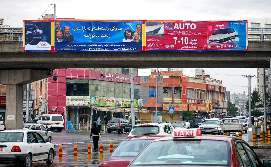 Large Power to Forgive campaign billboard spanning an overpass above city traffic in Erbil.