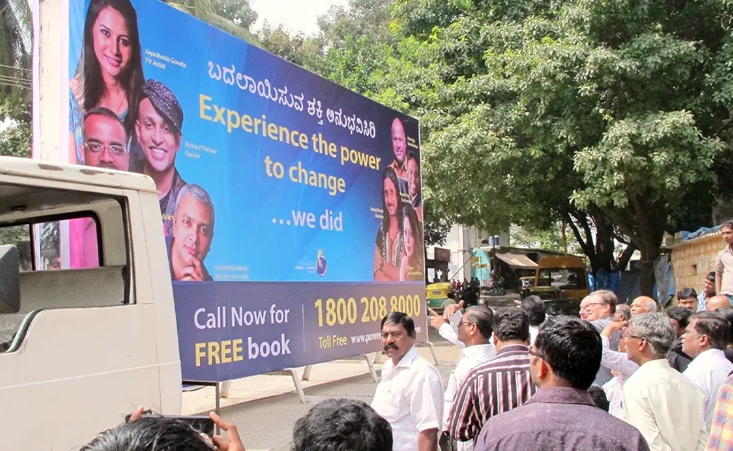 A large mobile billboard trailer with a “free book” campaign advertisement parked on a busy street as people gather nearby.