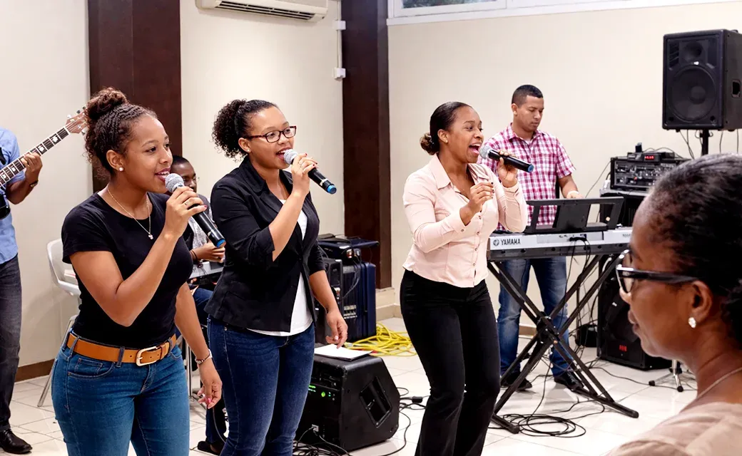 Three singers with microphones lead music while a keyboard player performs at a church gathering.