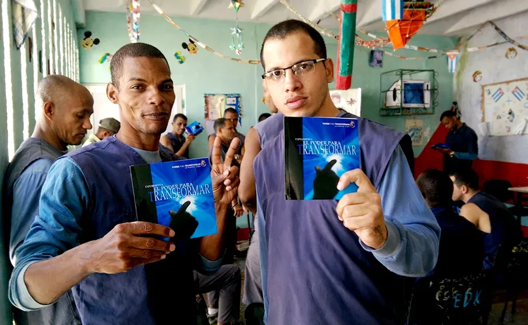 Two men indoors holding “El Poder para Transformar” books.