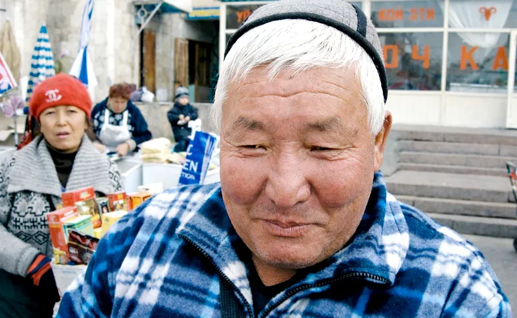 Close-up of a man in a market in Bishkek, Kyrgyzstan, with vendors and products in the background.