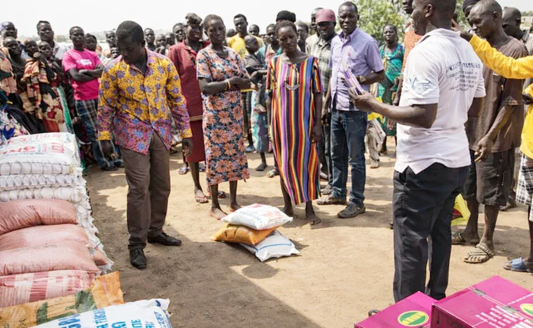 Stacks of food supplies and essentials set out for distribution as people gather nearby in Juba, South Sudan.
