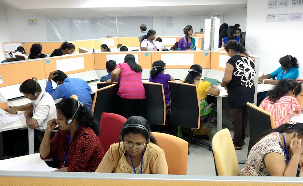 Call centre staff wearing headsets and working at desks in a large office.