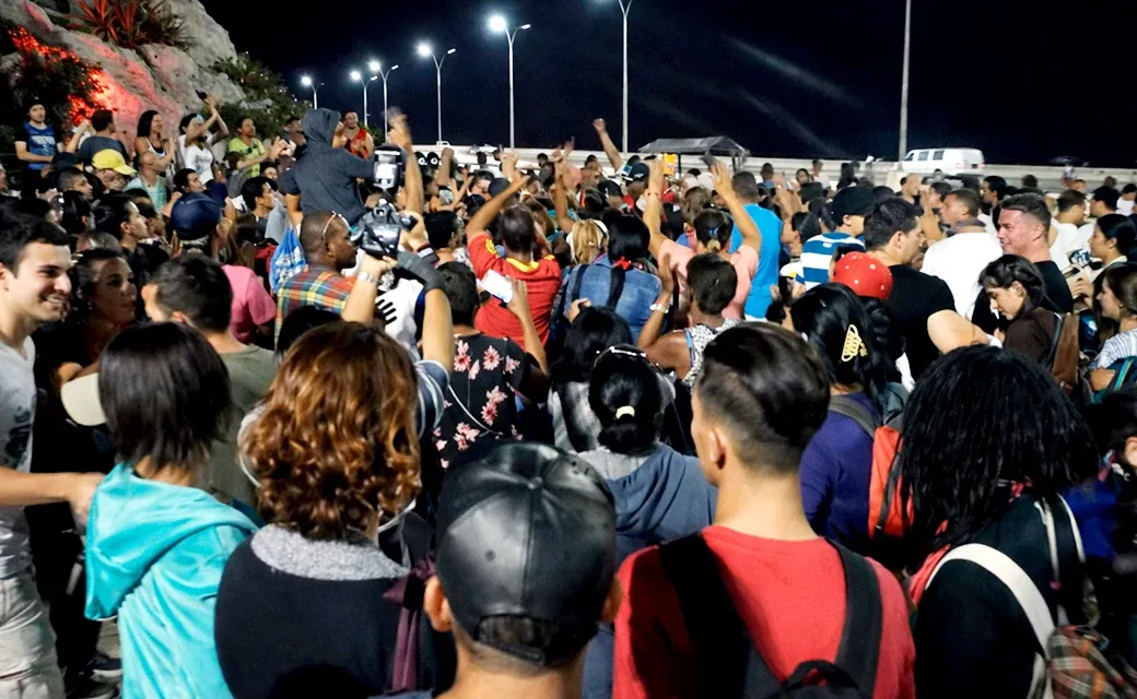 Crowd gathered outdoors at night with many hands raised.