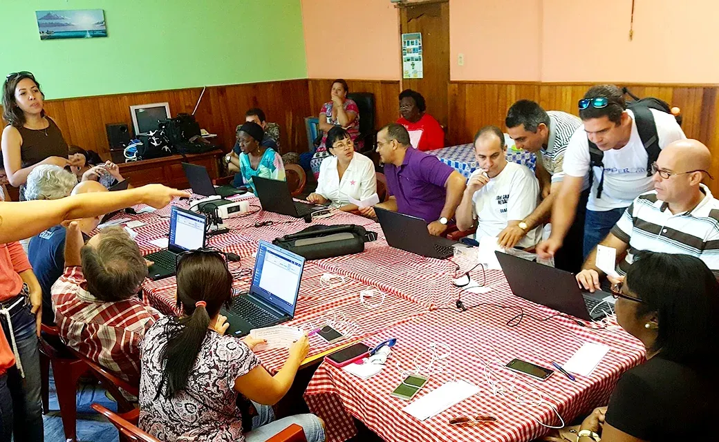 Group of volunteers seated around a table with laptops and papers during a call centre meeting.