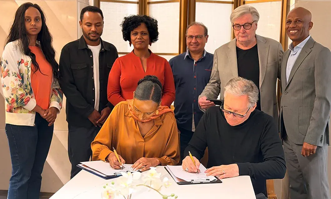 GCMM representatives and local partners gather around a table as two people sign partnership documents during a formal meeting.