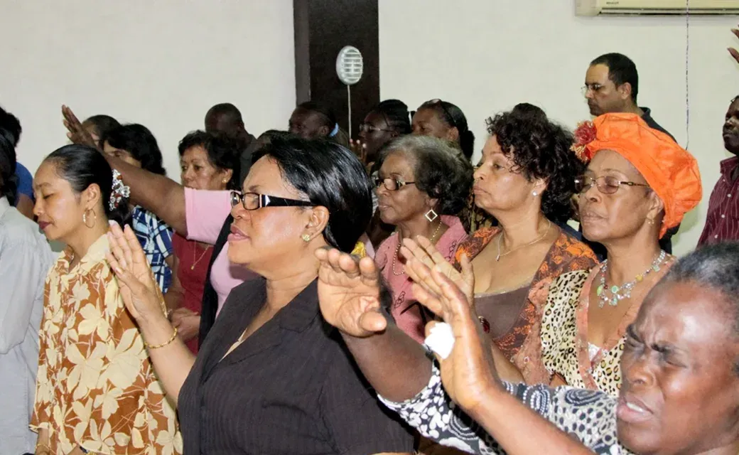 Congregation standing closely together with hands raised in prayer during a church gathering.