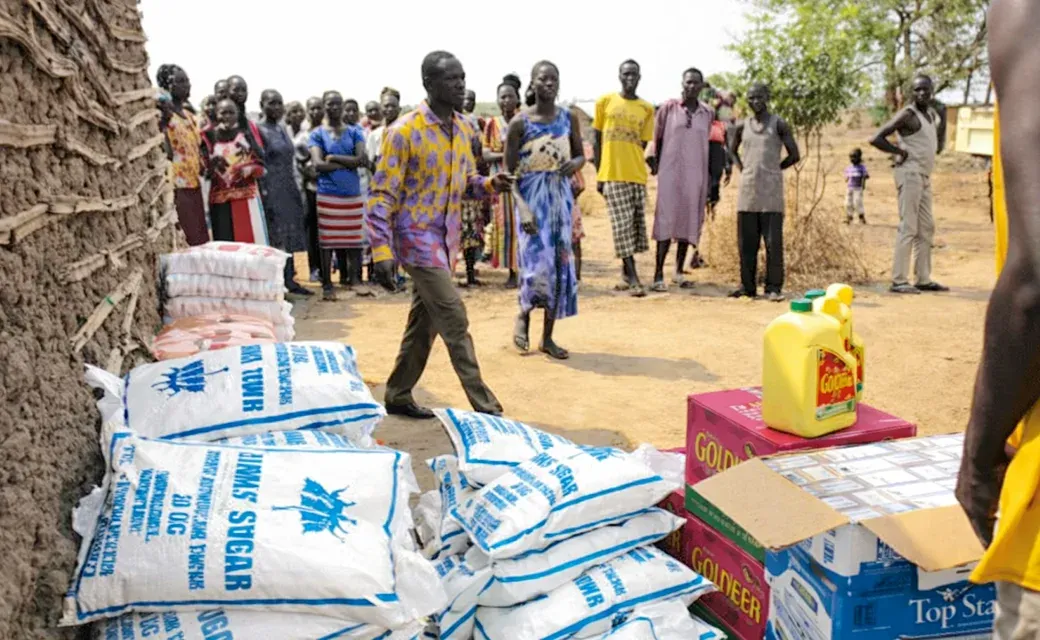 Stacks of food supplies and essentials set out for distribution as people gather nearby in Juba, South Sudan.