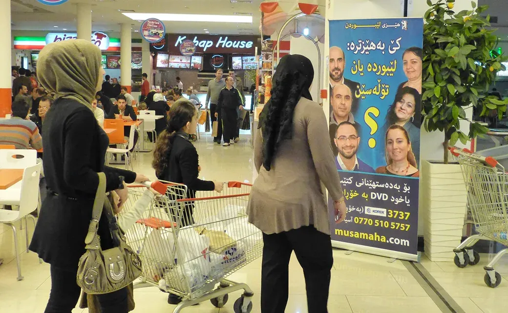 Shoppers in an Erbil mall pass a Power to Forgive campaign banner during the Mega City Media Campaign.