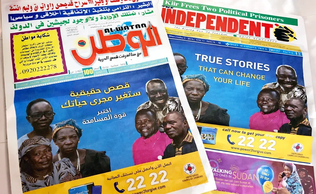 Two printed newspapers featuring South Sudan campaign stories and a call-to-action with a phone number and website.