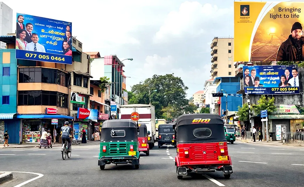 Busy Colombo street with tuk-tuks and two Mega City Media Campaign billboards visible on buildings.