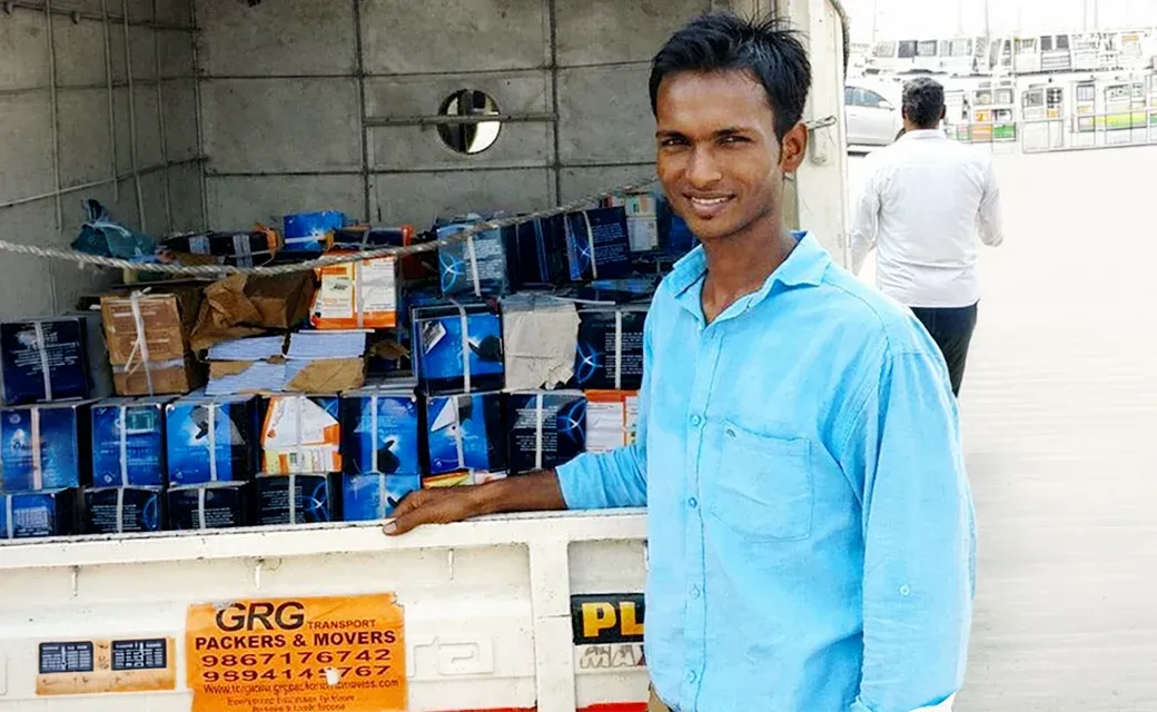 A man in a blue shirt stands beside a truck loaded with boxes of campaign books, preparing for distribution.