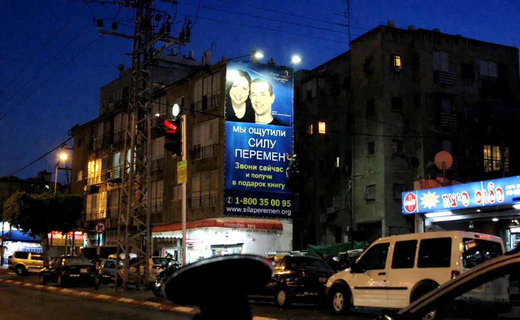 Large blue Russian-language campaign billboard lit above a city street at night