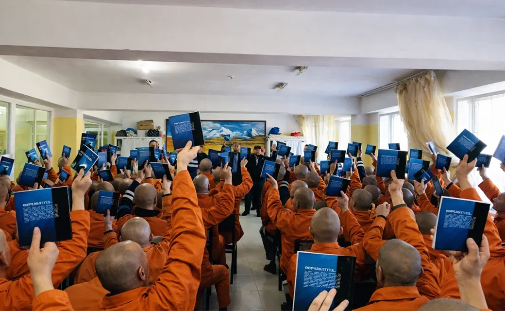 Inmates in Mongolia hold up mission books during a Mega City Media Campaign event.