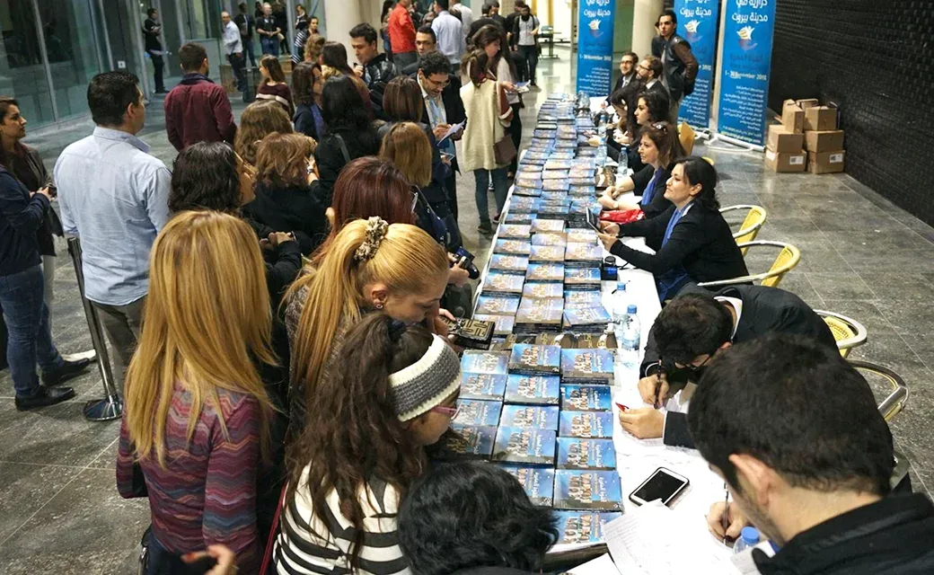 People queue at a long table covered with Arabic Power to Change books and DVDs while volunteers help attendees sign up.